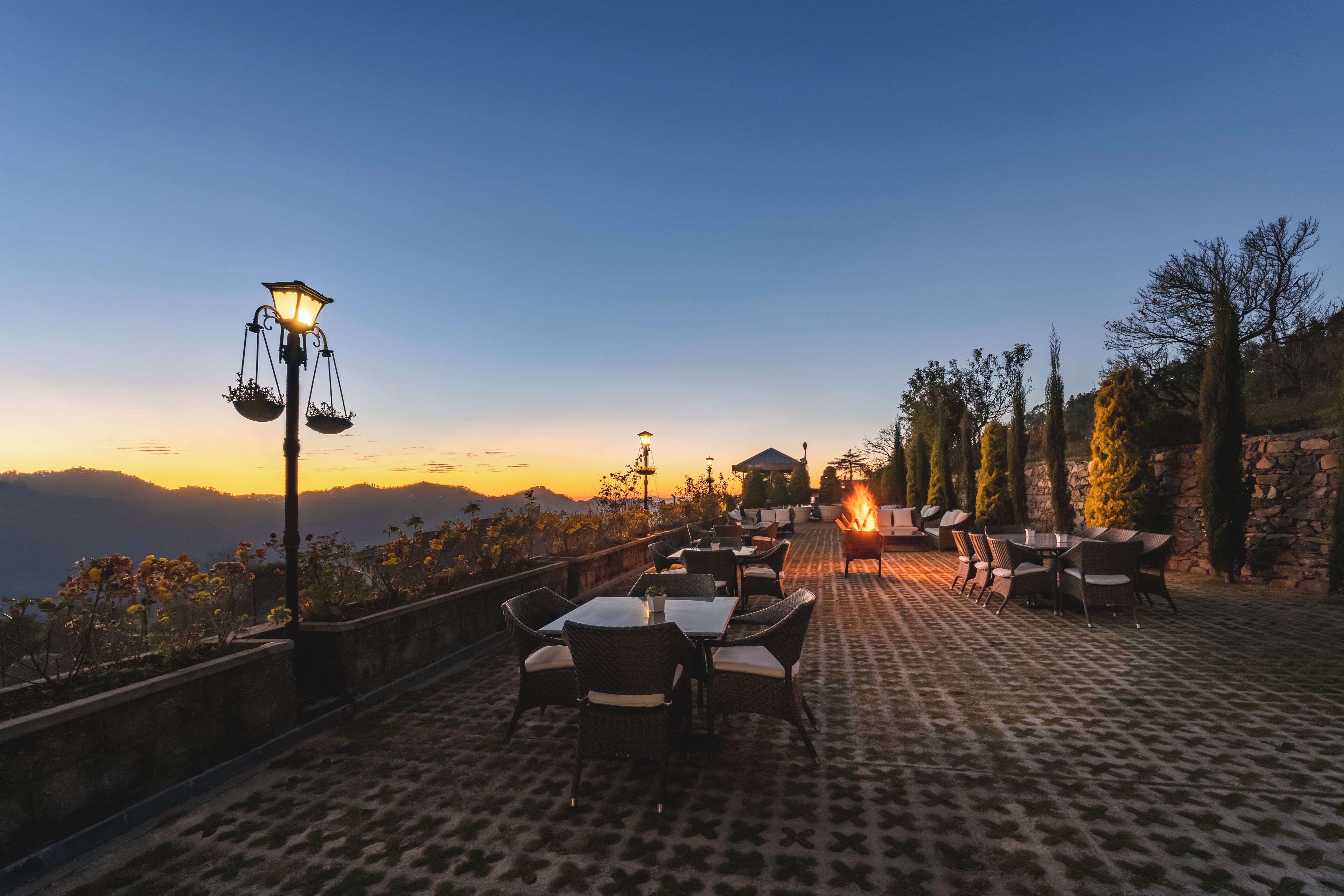 An outdoor terrace with tables and chairs, a stone wall, and a view of the mountains.