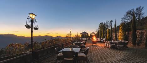 An outdoor terrace with tables and chairs, a stone wall, and a view of the mountains.