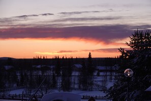 A snowy landscape with a sunset, a snow-covered house, and a Christmas tree. - Kierinki Village (Sodankyla)