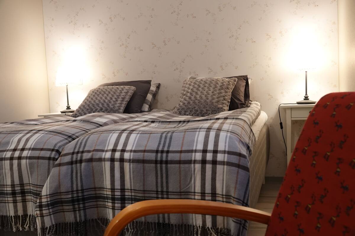 A bedroom with a double bed, two bedside tables, a lamp on each table, and a chair with a patterned cushion.