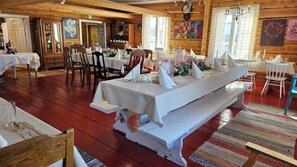 A dining area with a long white bench, multiple tables with white tablecloths, and chairs. - Kierinki Village (Sodankyla)