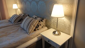 Un lit bien fait, agrémenté d’oreillers à rayures, une lampe de chevet et un papier peint à motifs floraux.
