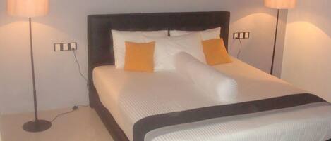 A neatly made bed with white and orange bedding, flanked by two bedside lamps on either side.