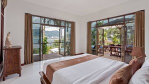 Ein geräumiges Schlafzimmer mit einem großen Bett, einer Statue und Blick auf einen Balkon mit Gartenmöbeln.