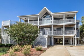 A two-story house with a covered front porch, a staircase leading to the upper level, and a large tree in the front yard. - Lucy's Place | 1030 ft from the beach | Private Pool, Hot Tub | Southern Shores (Southern Shores)