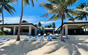 A beachfront property with multiple lounge chairs and palm trees.