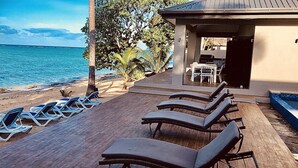 A beachside lounge with sun loungers and a pool area, overlooking the sea.