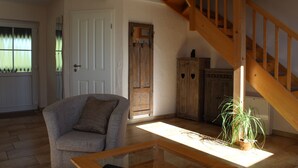 Een woonkamer met een houten trap, een grijze fauteuil, een houten kast en een kamerplant.