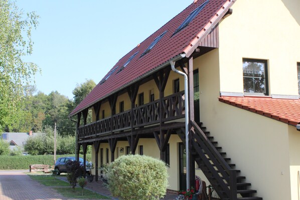 A building with a red-tiled roof, wooden balcony railings, and a staircase leading to the entrance.