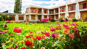 Ein Hotel mit mehreren Balkonen, einem Garten voller farbenfroher Blumen und einem strahlend blauen Himmel.