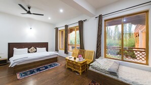 Ein Schlafzimmer mit einem Bett, einer Holzbank, einem kleinen Tisch und großen Fenstern mit Vorhängen.