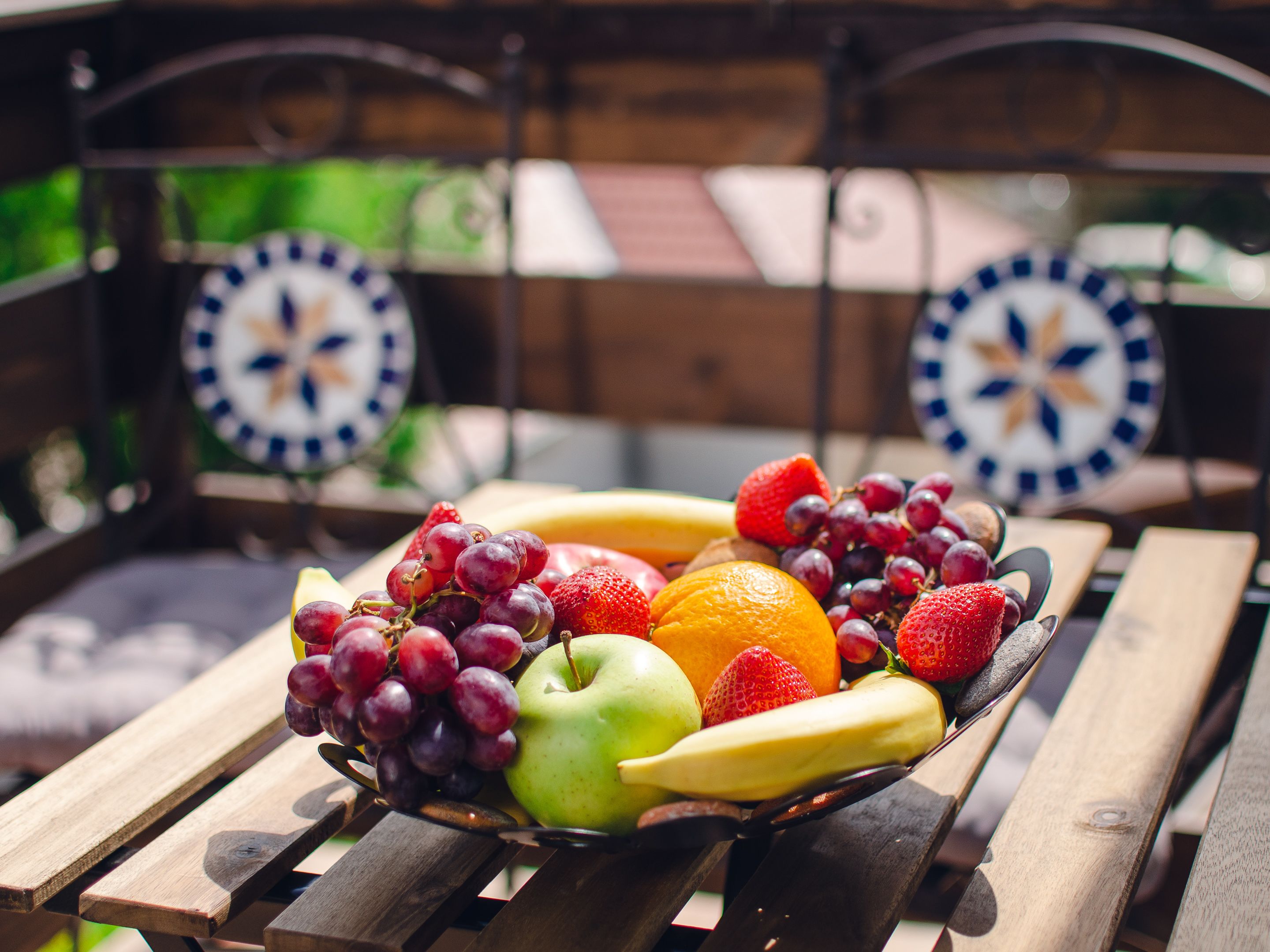 A wooden table with a fruit bowl containing grapes, strawberries, an apple, a banana, and an orange.