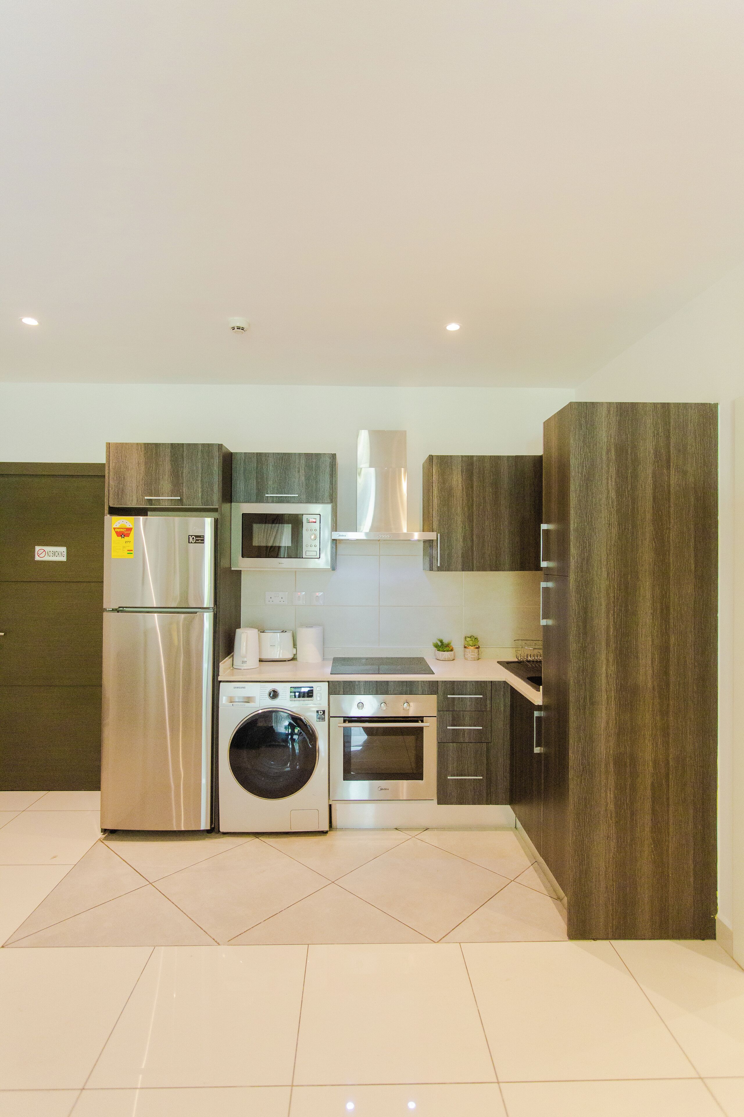 A modern kitchen with stainless steel appliances, a built-in washing machine, and dark wood cabinetry.