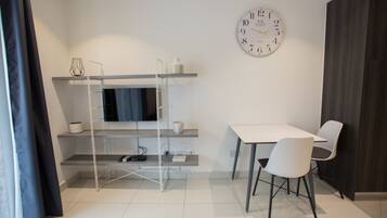 Una habitación moderna con una televisión en un estante, una mesa de comedor con sillas y un reloj de pared grande.