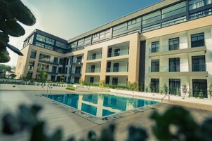 A modern building with a swimming pool, multiple balconies, and a clear sky.