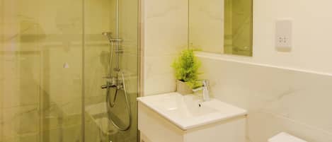 Un baño moderno con ducha de vidrio, lavamanos blanco, espejo y retrete.