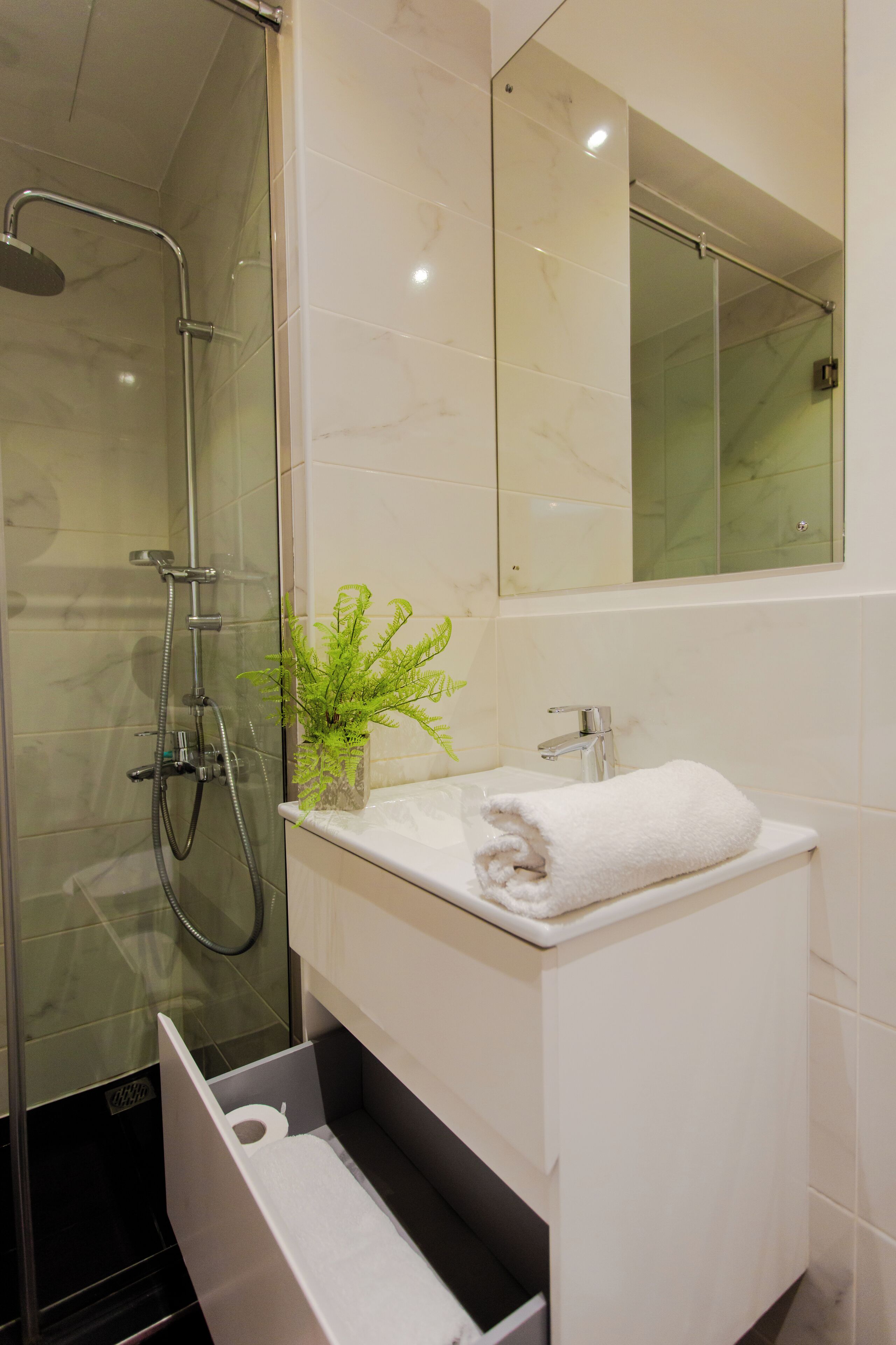 Un bagno moderno con doccia vetrata, lavandino bianco con asciugamano e specchio sopra.