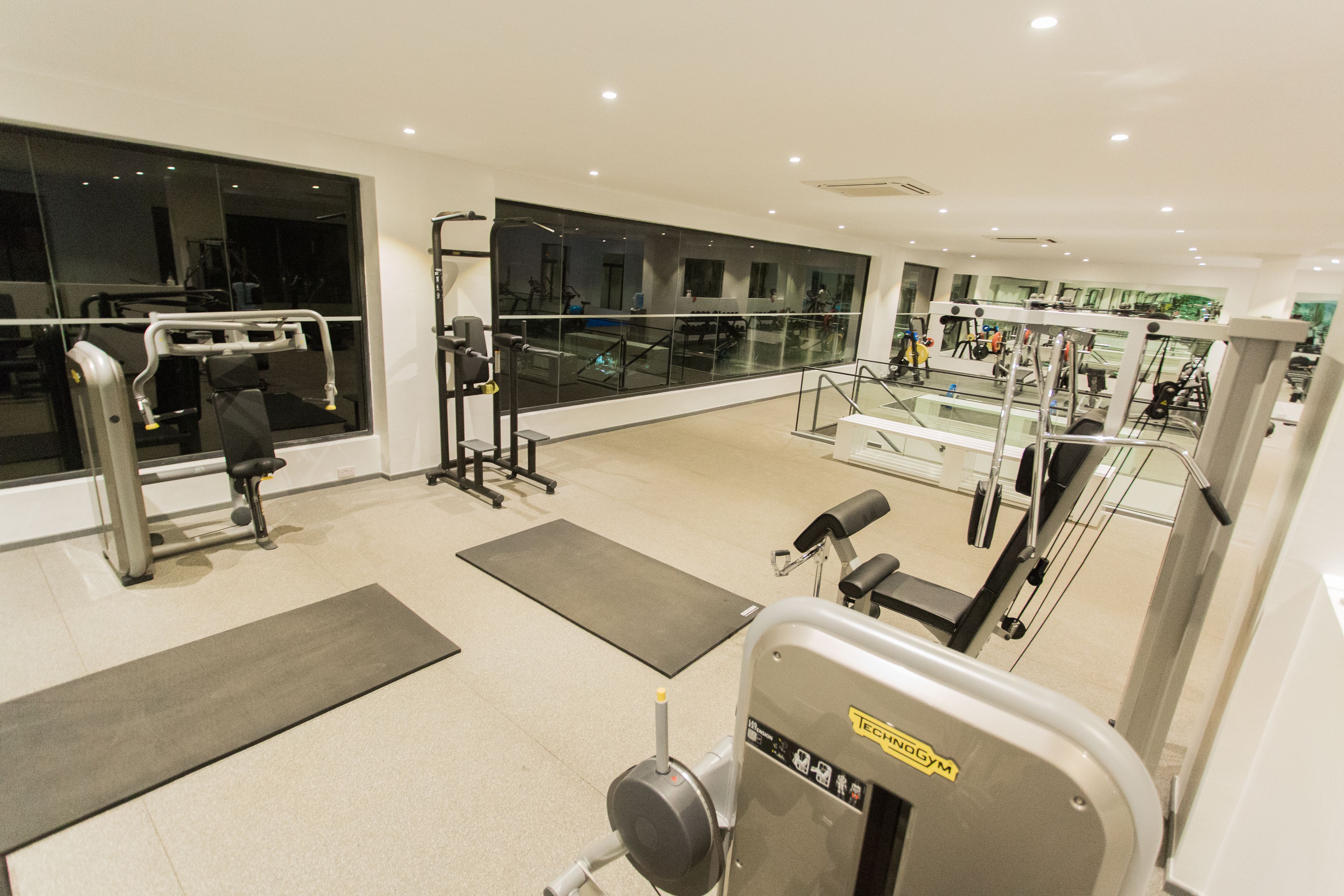 A modern gym with various exercise machines, large windows, and a clean, spacious layout.
