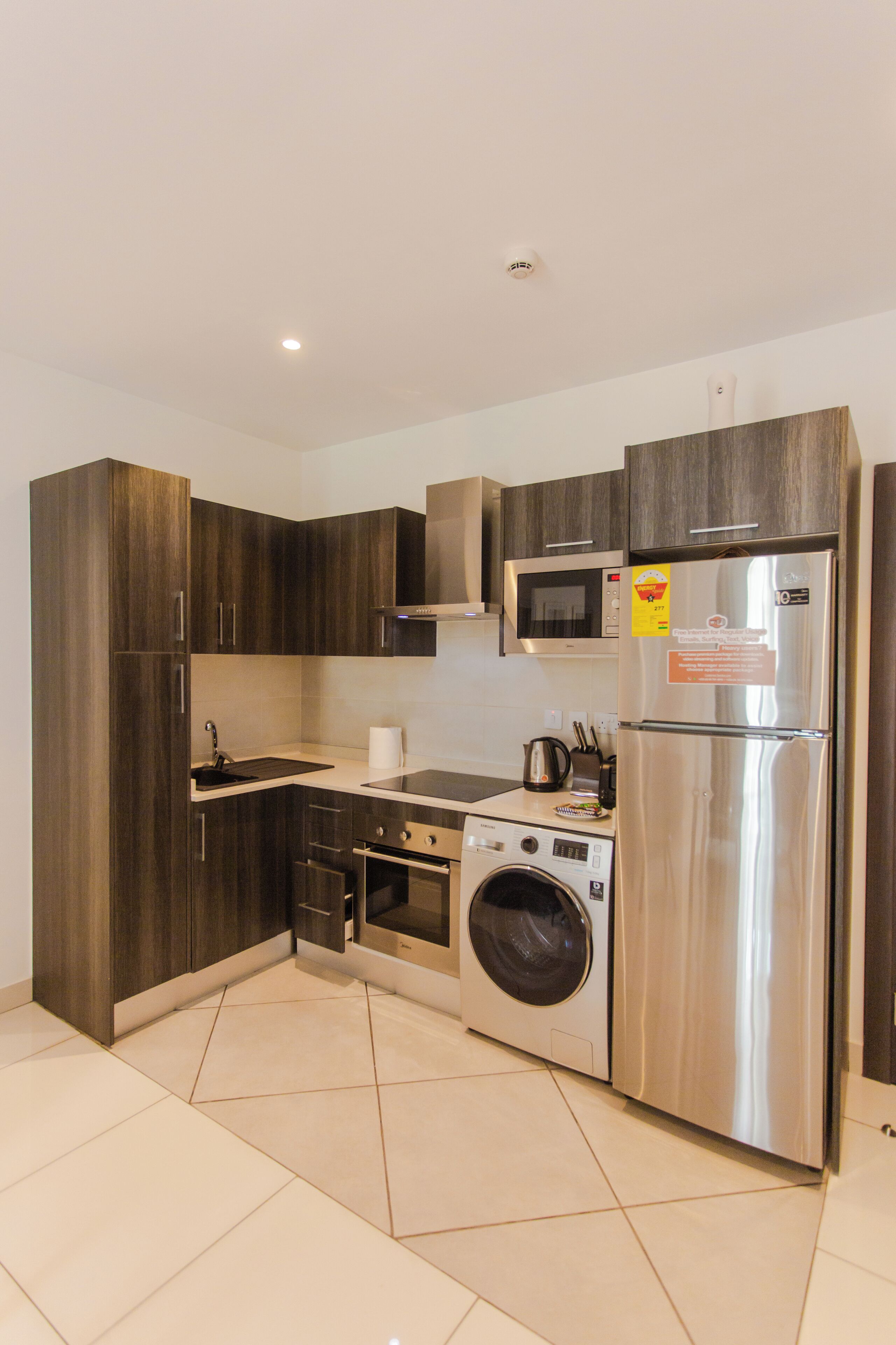 Una cocina moderna con armarios de madera oscura, electrodomésticos de acero inoxidable, microondas integrado y lavadora.