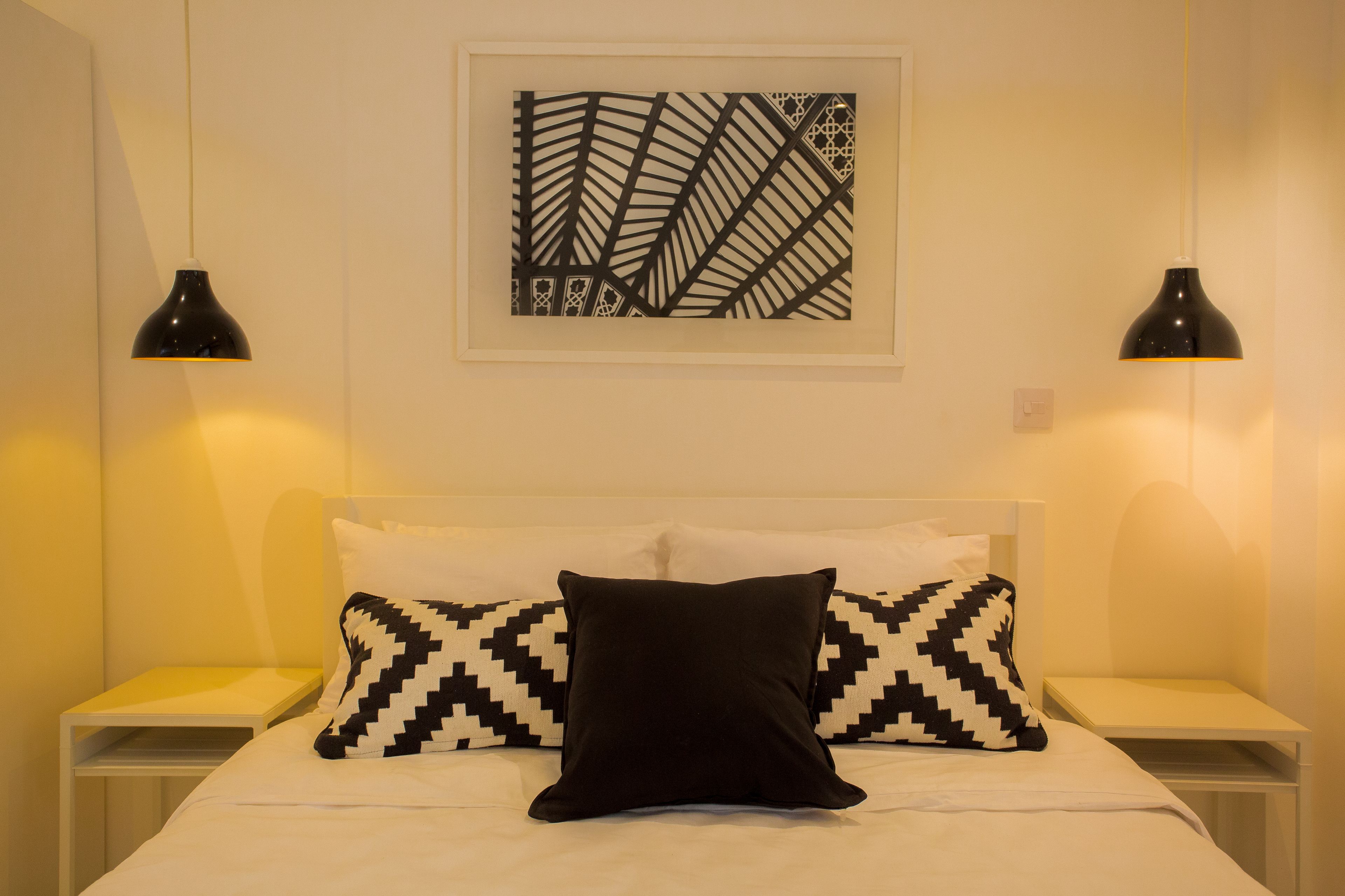 Une chambre d’hôtel bien rangée, avec un lit, deux tables de chevet et une œuvre d’art accrochée au mur.