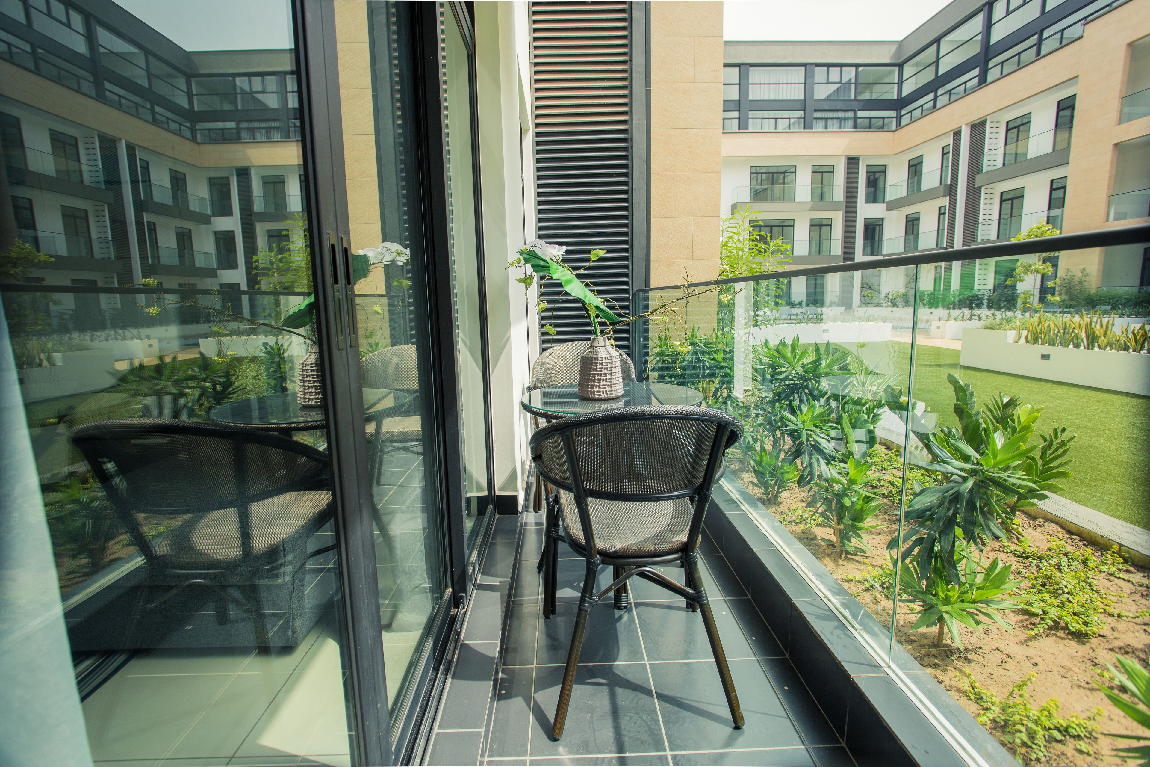 Un balcon avec une porte vitrée, une chaise en osier, une petite table et un pot de fleurs.