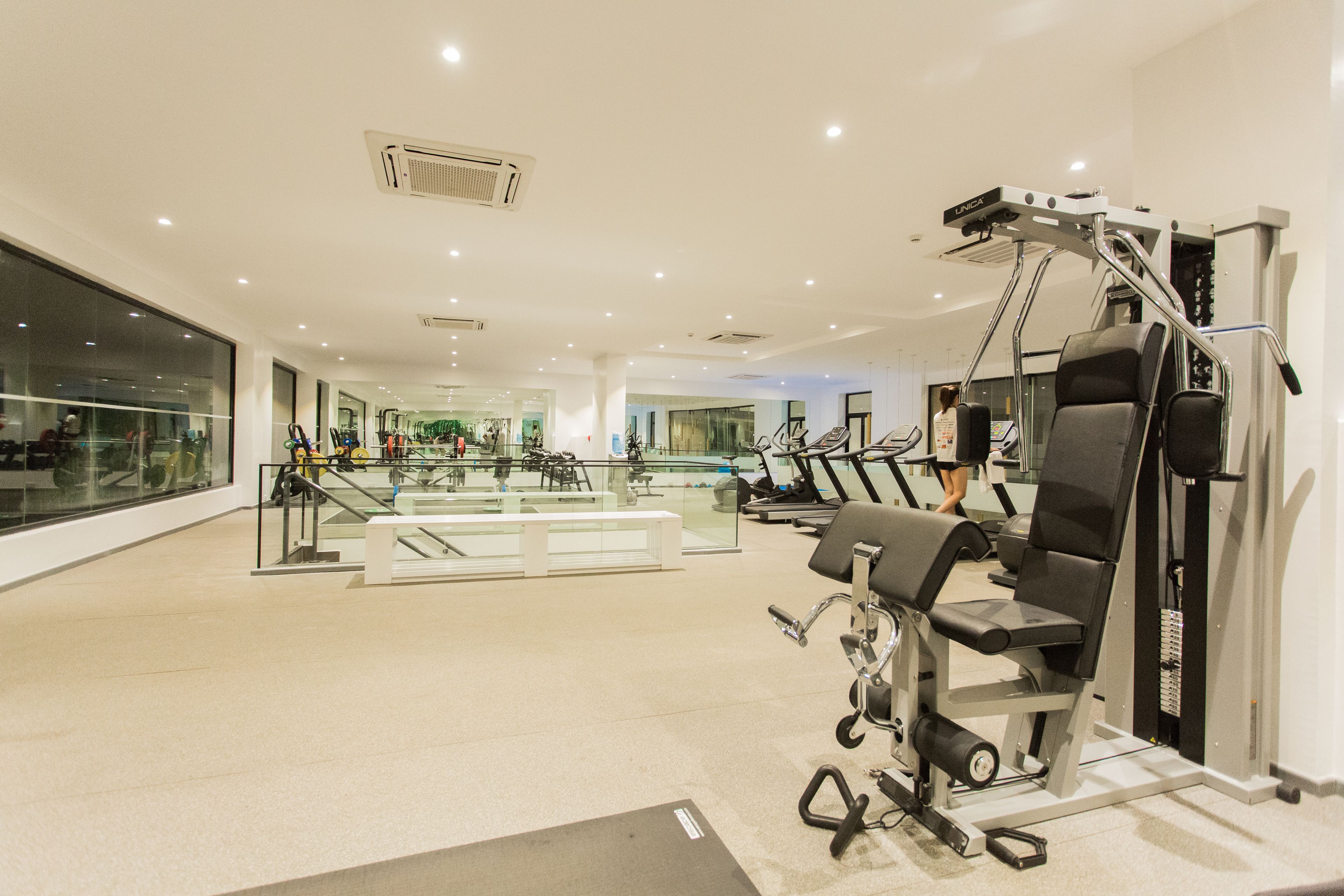 Ein modernes Fitnessstudio mit verschiedenen Trainingsgeräten, einer Glaswand und großzügigem Raumangebot.