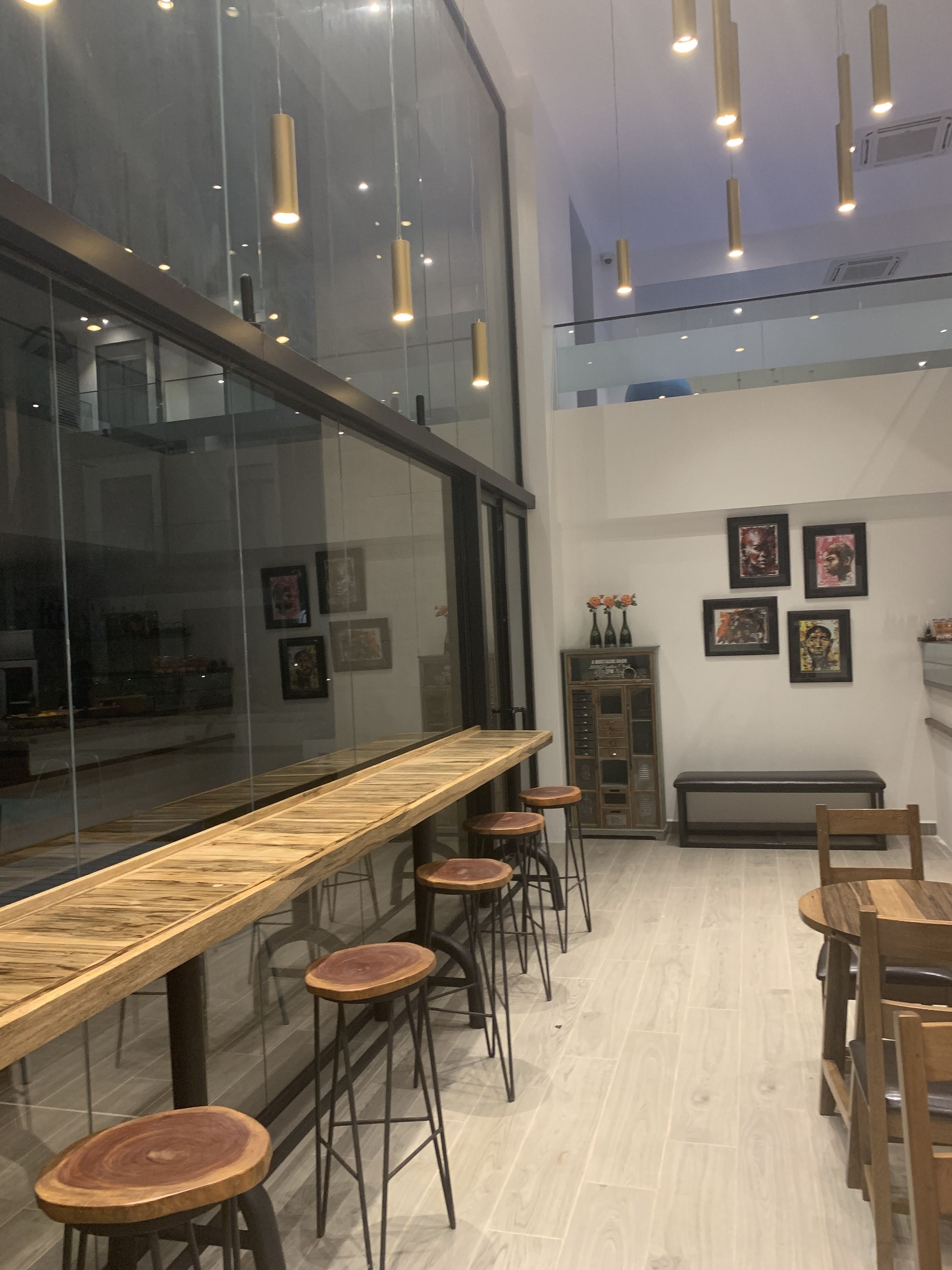 A modern interior with a long wooden bar, bar stools, and a seating area with wooden tables and chairs.