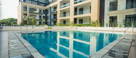 A modern building with a swimming pool, multiple balconies, and a garden area.