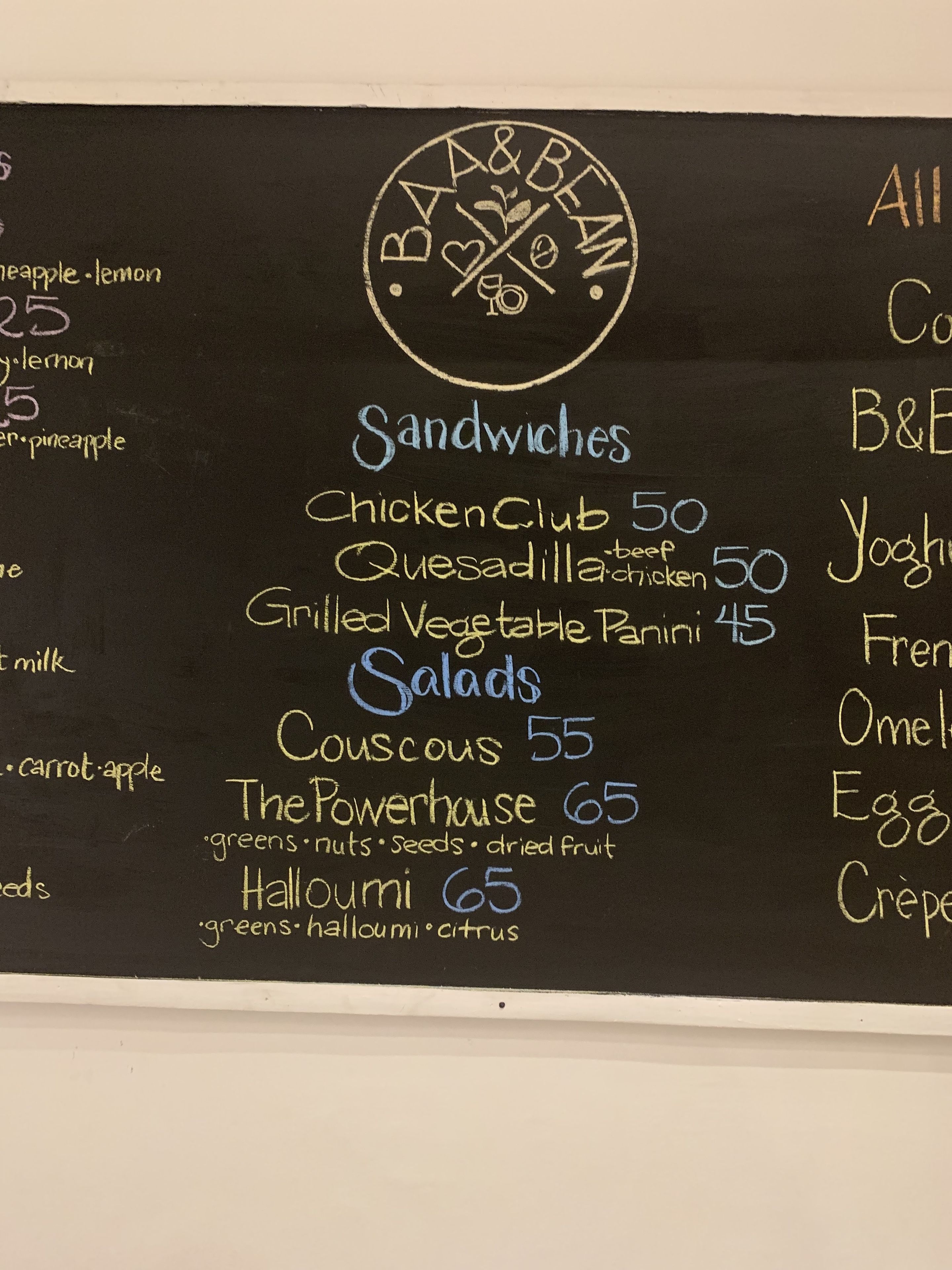 A chalkboard menu listing sandwiches, salads, and other items with prices.