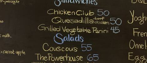 A chalkboard menu listing sandwiches, salads, and other items with prices.