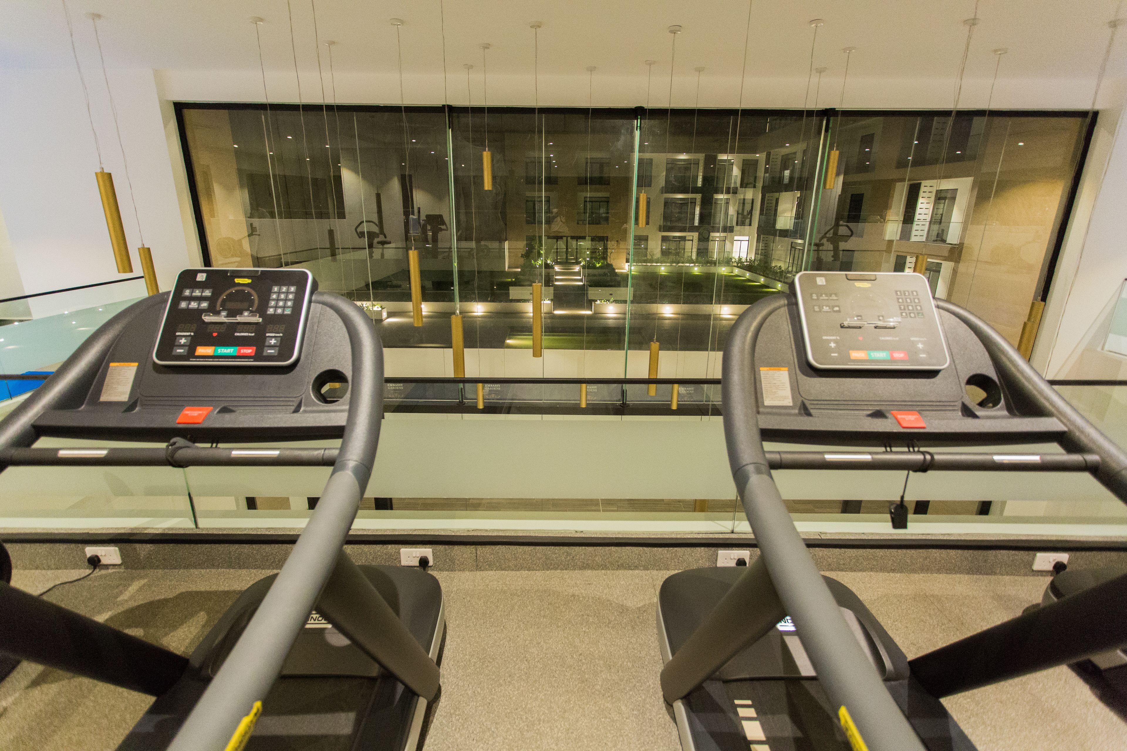 A treadmill with a digital display, positioned in front of a large window overlooking a building.