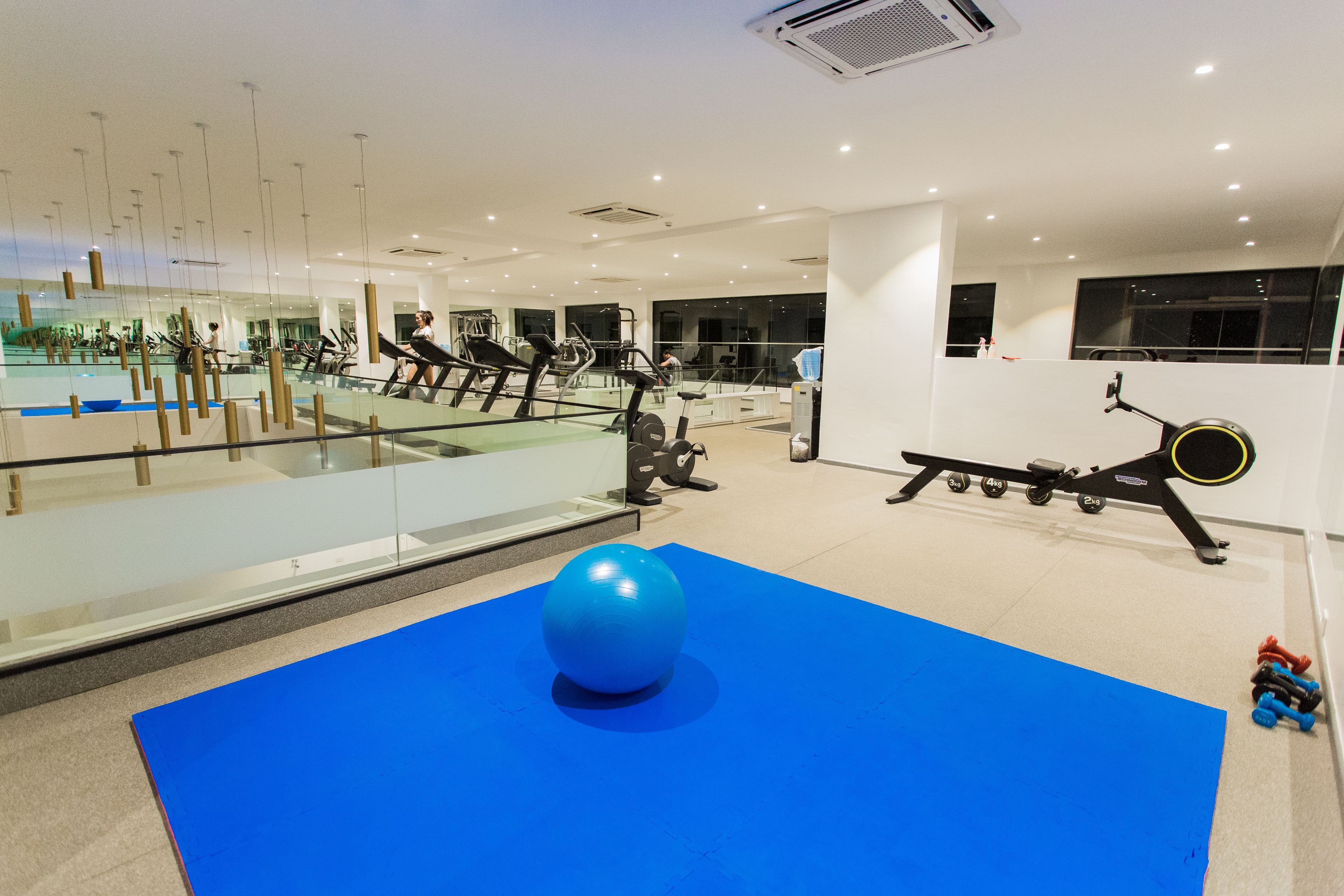 Een moderne sportschool met trainingsapparatuur, een grote blauwe mat en een glazen wand die het interieur weerspiegelt.