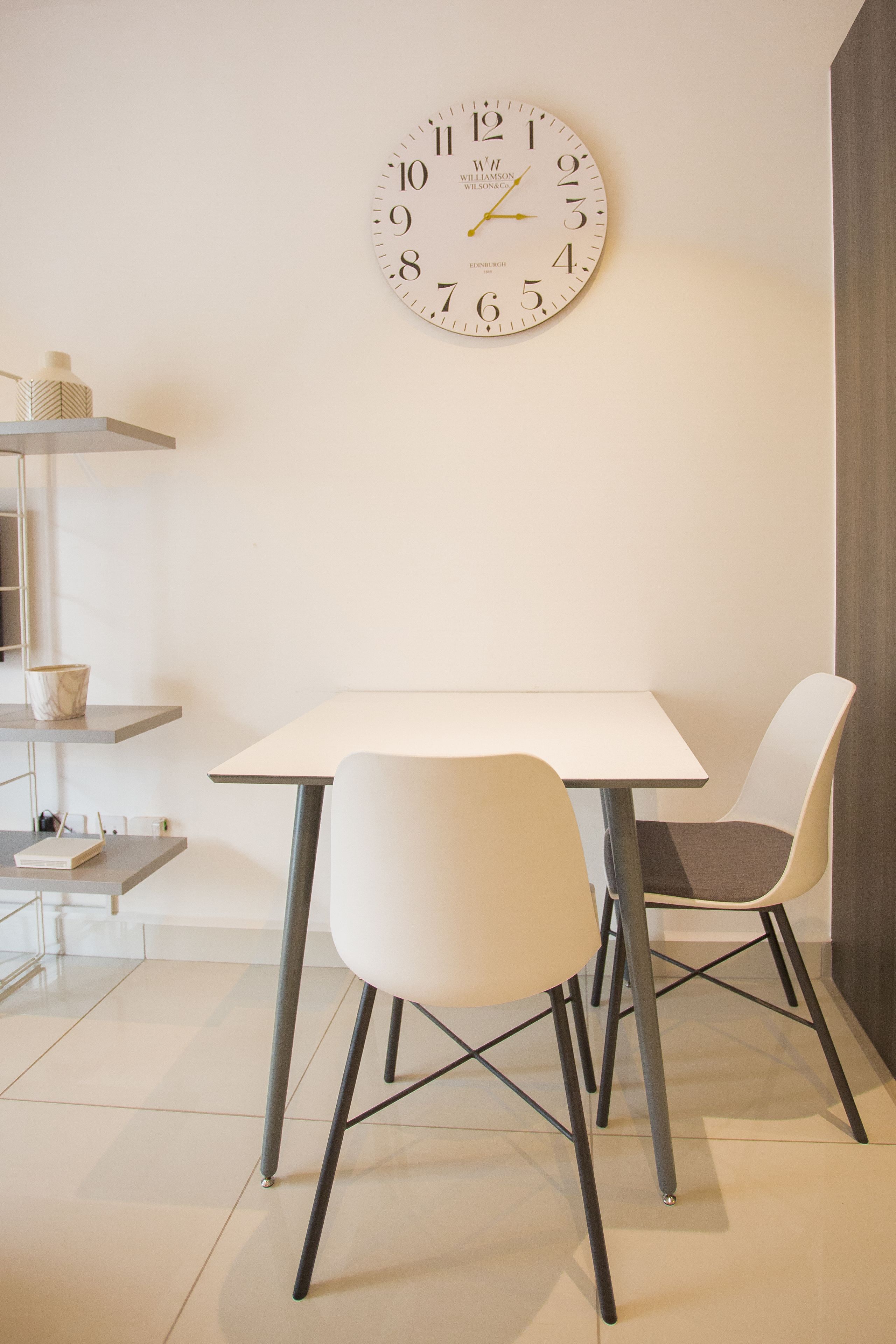 A dining area with a white table, two chairs, and a wall clock.