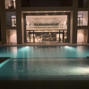 Une piscine avec vue sur un bâtiment abritant un bar et un espace salon.