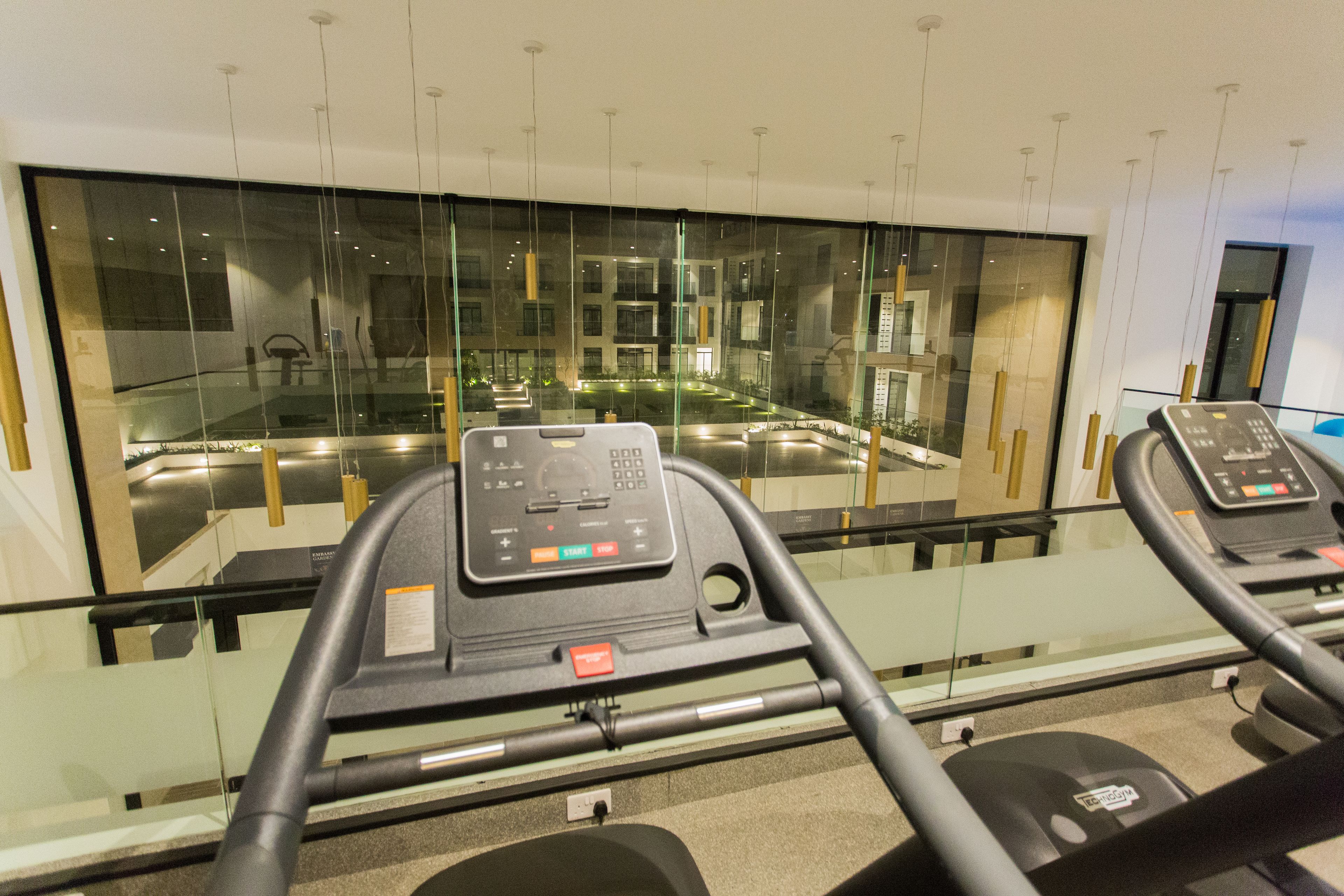 A treadmill with a control panel, a glass window, and a reflection of a building's interior.