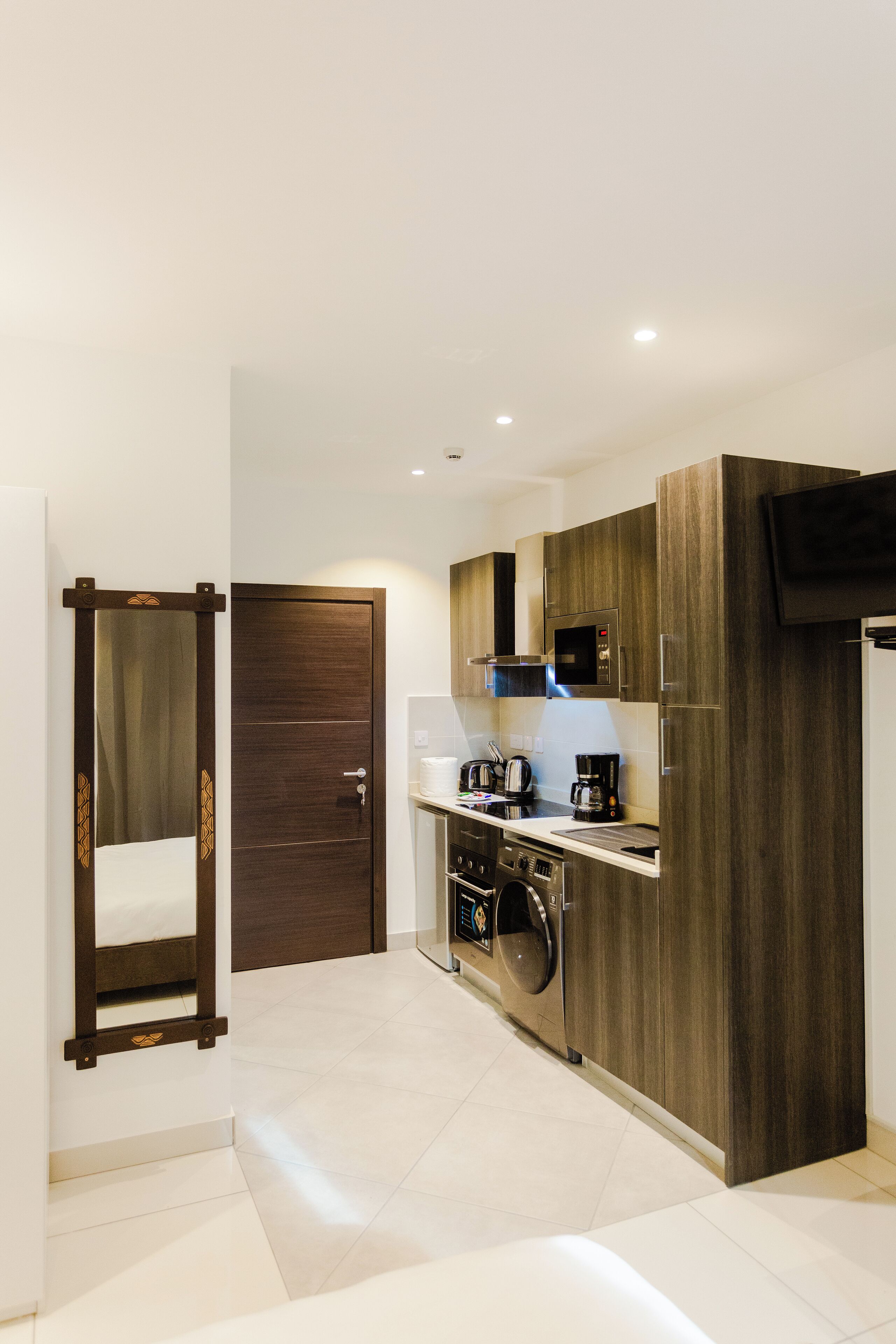 A modern kitchen with wooden cabinets, a microwave, a coffee maker, and a washing machine.