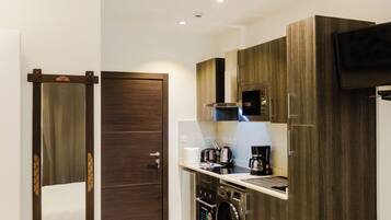 A modern kitchen with wooden cabinets, a microwave, a coffee maker, and a washing machine.