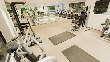 A modern gym with various exercise equipment, a glass wall offering a view of the city, and a spacious layout.