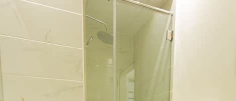 A modern bathroom with a glass shower enclosure, white tiles, a black rug, and two white towels on the wall.