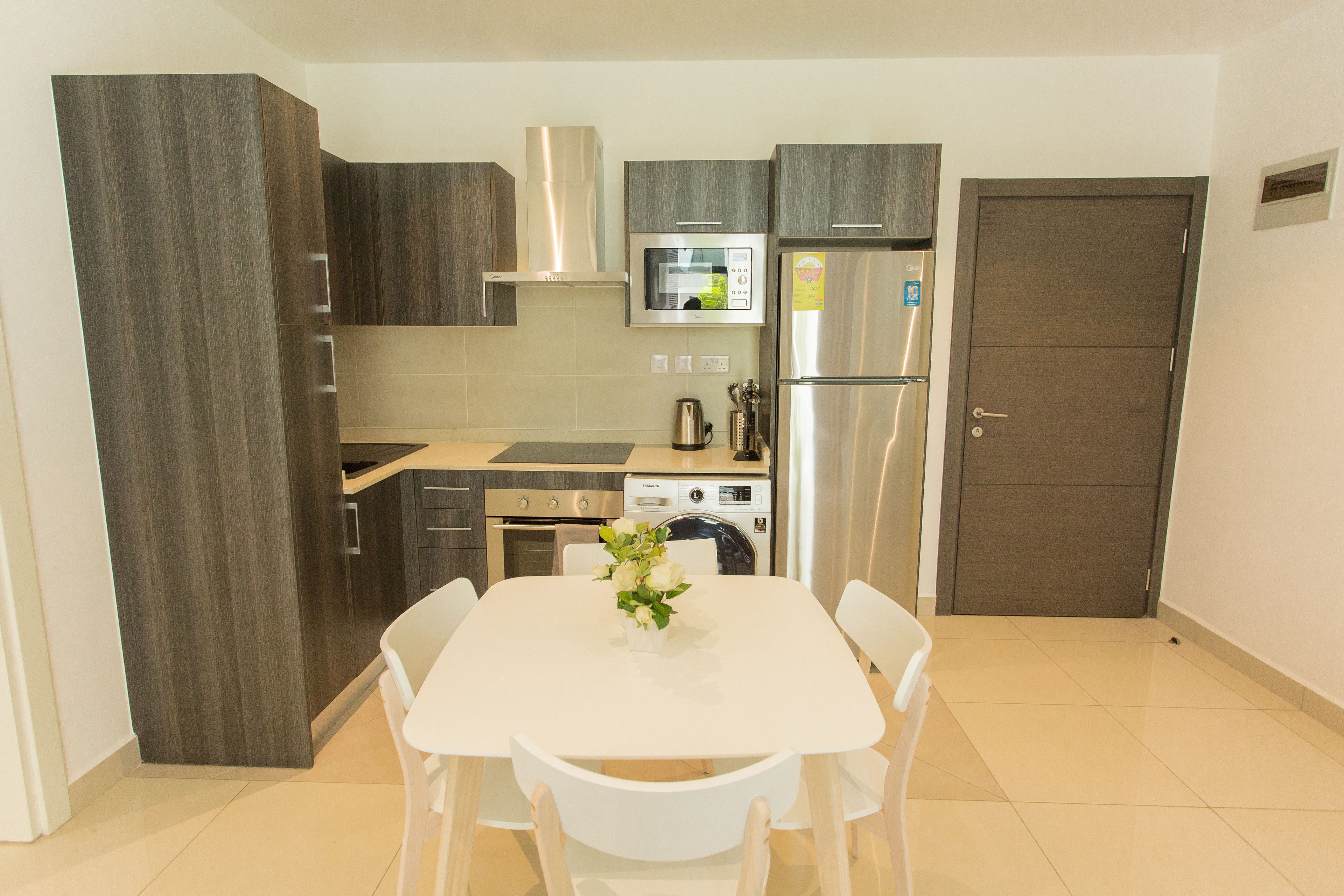 A modern kitchen with dark wood cabinets, stainless steel appliances, and a white dining table with chairs.