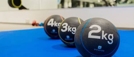 Tres pelotas de ejercicio marcadas con pesas sobre una colchoneta azul en un gimnasio.