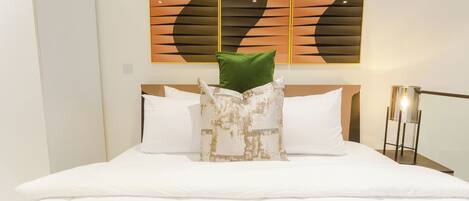 A hotel room with a neatly made bed, a modern abstract painting on the wall, and a bedside table with a lamp.