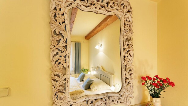 Un miroir avec un cadre orné, un lit avec des oreillers et un vase rempli de fleurs.