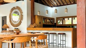 A modern kitchen with wooden cabinets, a dining area with a wooden table and chairs, and hanging pendant lights.