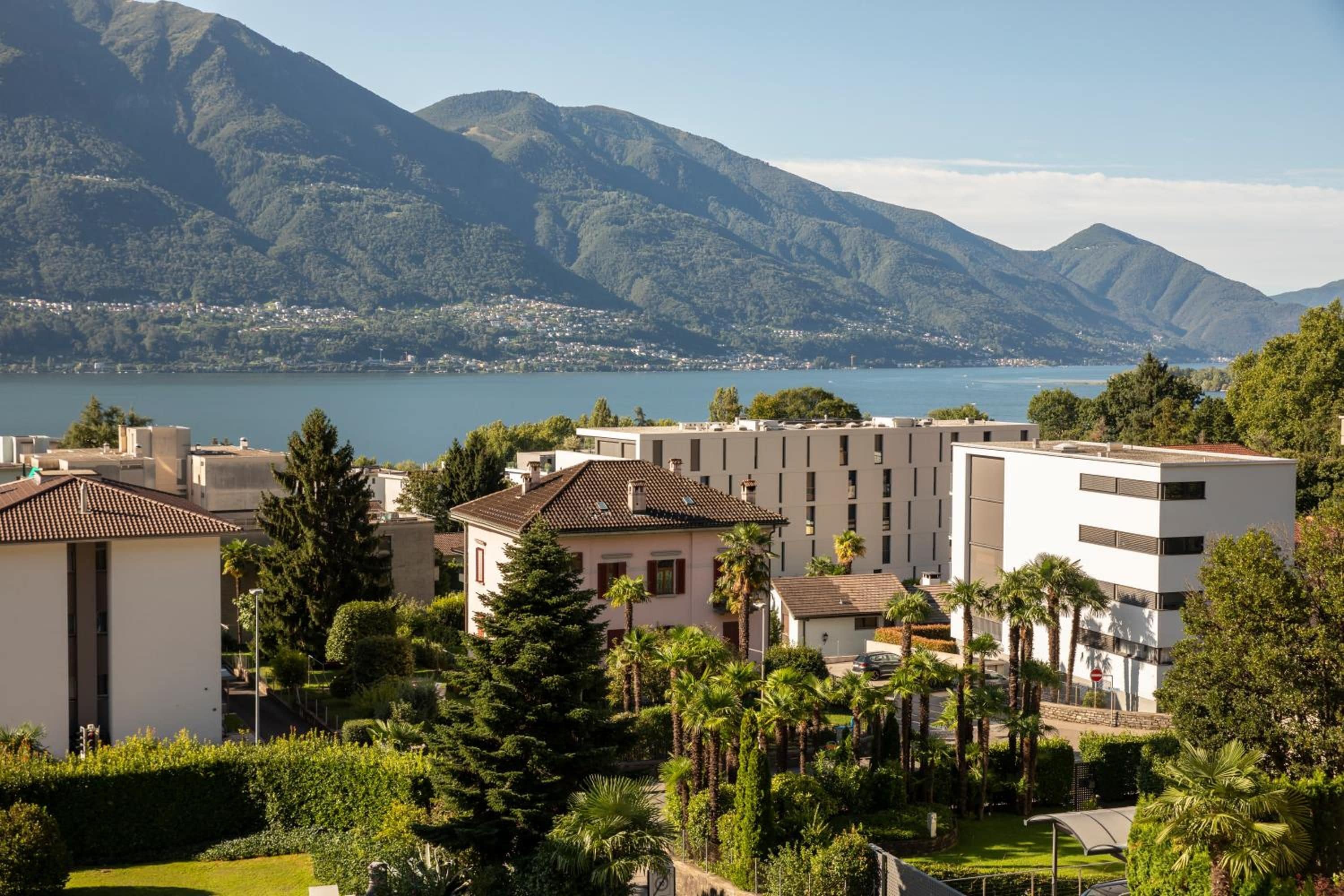 Un quartier résidentiel avec des bâtiments modernes, un lac et des montagnes en arrière-plan.