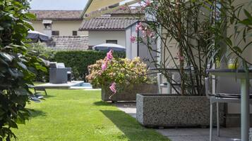 Un giardino con un vaso in cemento, un prato e un edificio con tetto in tegole sullo sfondo.