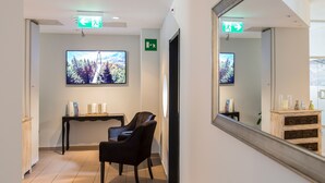 A modern interior with a black leather chair, a wooden table with books and candles, a large flat-screen TV, and a mirror reflecting the room. - Smart-HOTEL MINUSIO, a Swiss Quality Hotel (Minusio)