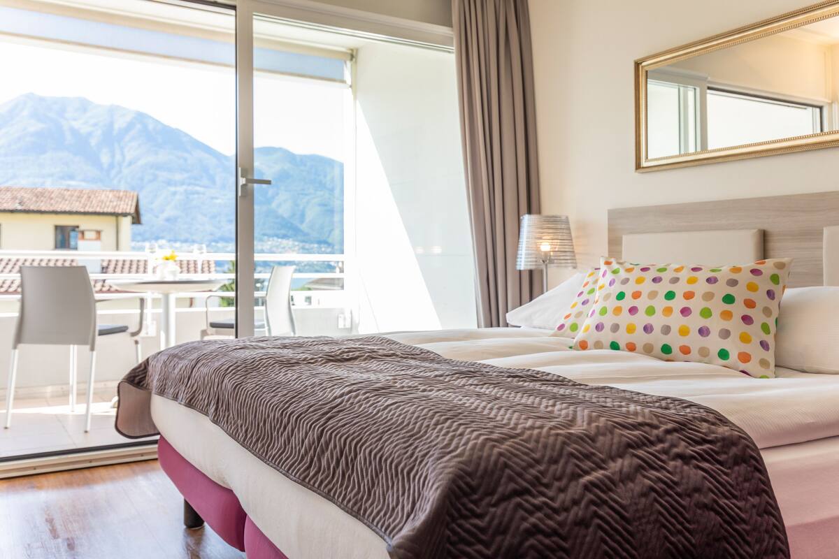 Une chambre d’hôtel avec un lit, une fenêtre donnant sur les montagnes, une chaise et une table avec vue.