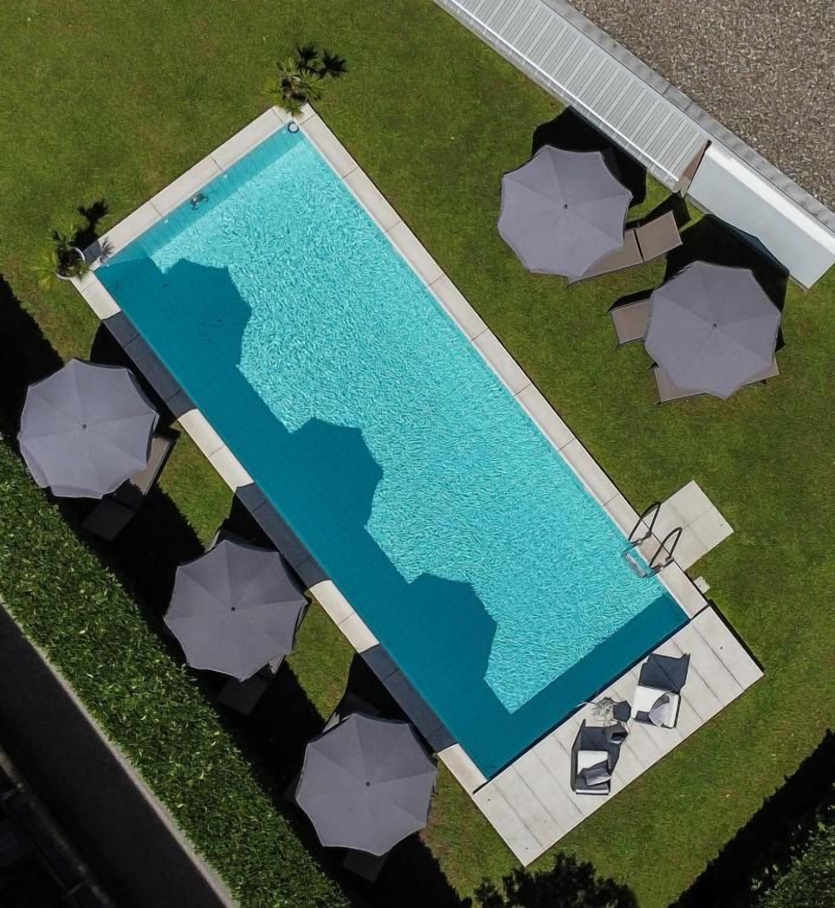 Ein rechteckiger Pool mit einer umlaufenden Sonnenterrasse, Sonnenschirmen und Liegestühlen.