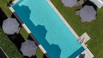 Ein rechteckiger Pool mit einer umlaufenden Sonnenterrasse, Sonnenschirmen und Liegestühlen.